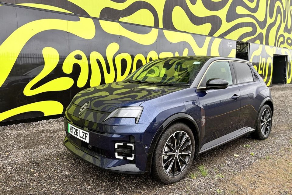 Dark blue Renault Megane E-Tech electric car parked on gravel in front of a black and yellow patterned wall
