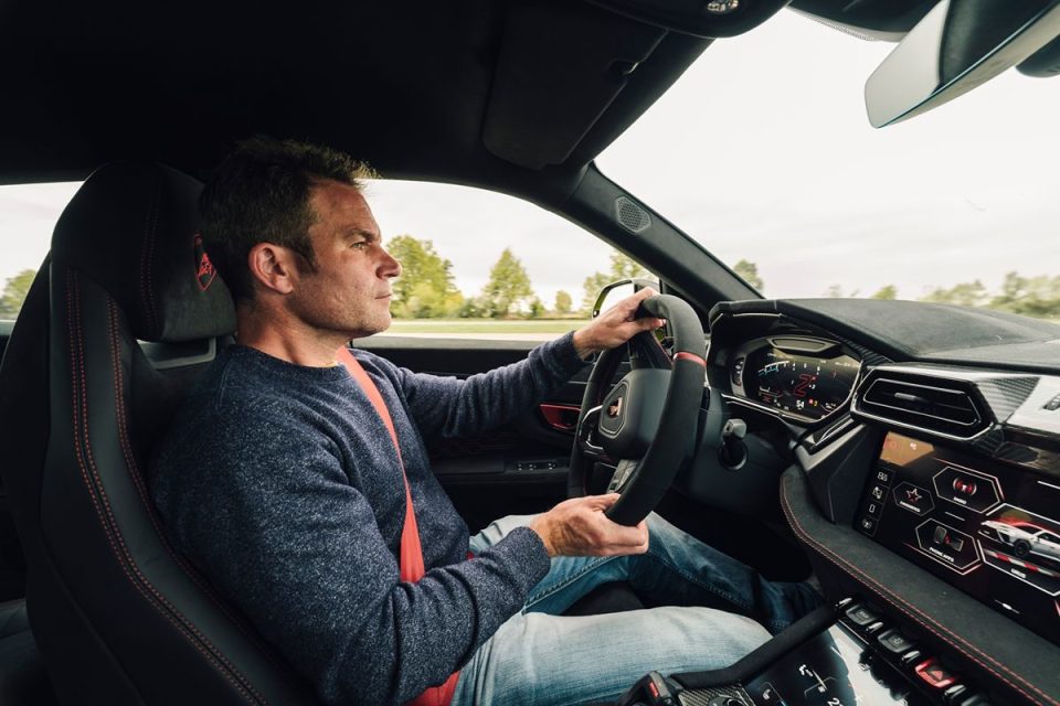 Man driving a high-performance luxury car with a red seatbelt and modern digital dashboard