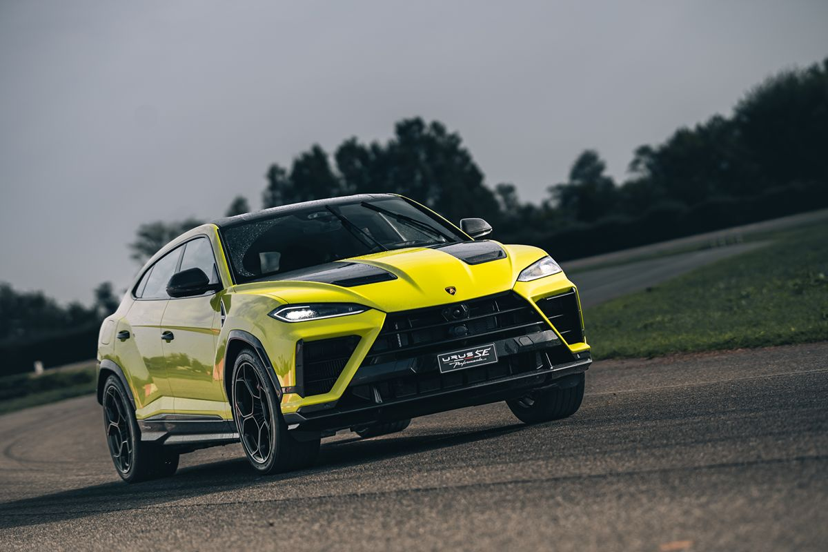 Bright yellow Lamborghini Urus SE SUV on a wet asphalt road, dark sky and trees in background