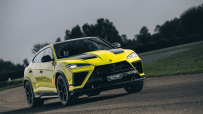 Bright yellow Lamborghini Urus SE SUV on a wet asphalt road, dark sky and trees in background