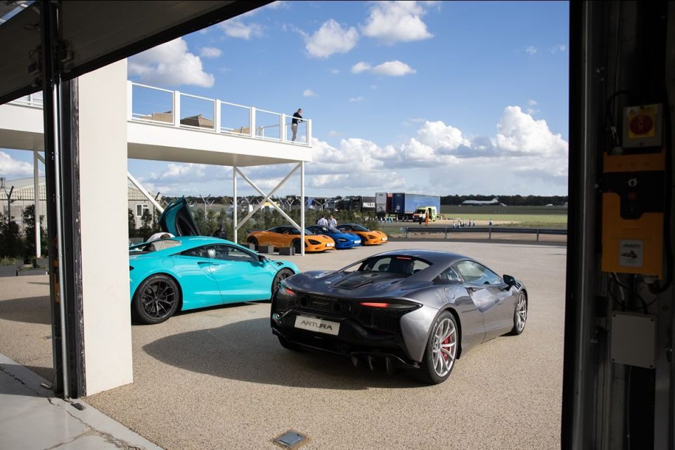 Multiple McLaren Artura sports cars, including a gray and a blue model, parked at an outdoor event