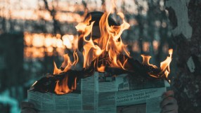 Hands holding a burning newspaper, symbolizing information wars and local news on fire