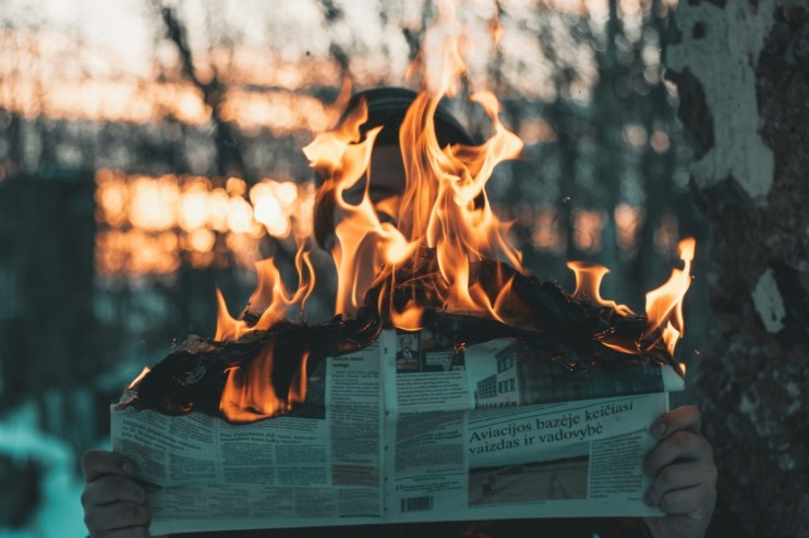 Hands holding a burning newspaper, symbolizing information wars and local news on fire
