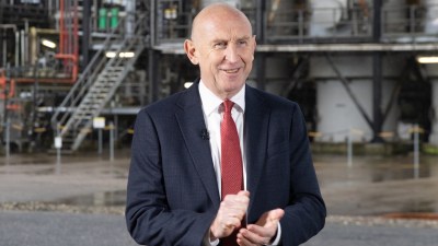 John Healey, Chancellor of the Exchequer, smiling and clapping in a dark suit and red tie.
