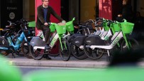Man on a Lime e-bike, surrounded by other Lime and Forest rental bikes on a city pavement.