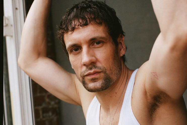 Nick Blood, an actor, looking directly at the camera while wearing a white tank top.