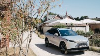 Silver Omoda 7 SUV parked on a gravel path next to brick buildings and white patio umbrellas