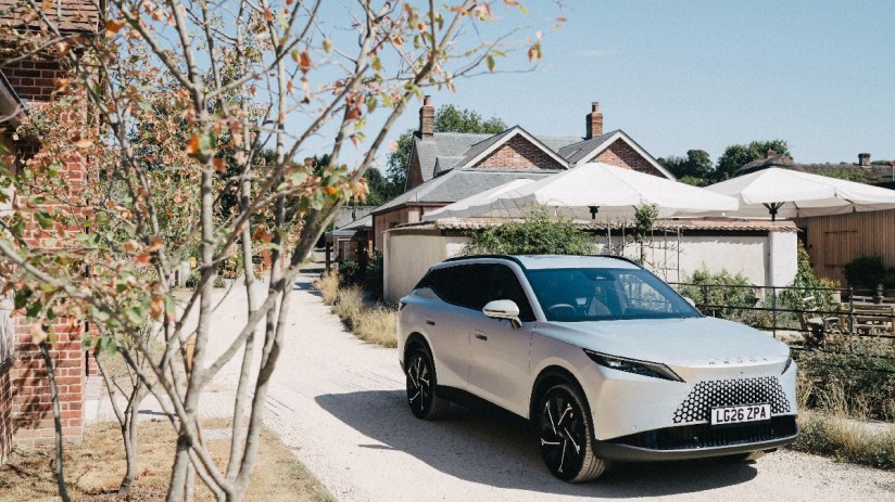 Silver Omoda 7 SUV parked on a gravel path next to brick buildings and white patio umbrellas