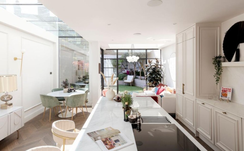 Modern kitchen and dining area with skylight, white marble island, and green velvet chairs in Peckham home.