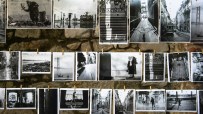 Black and white photographs displaying urban scenes, street photography, and landscapes hanging on a stone wall