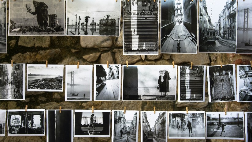 Black and white photographs displaying urban scenes, street photography, and landscapes hanging on a stone wall