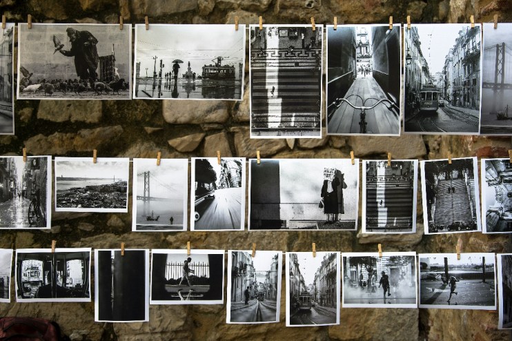 Black and white photographs displaying urban scenes, street photography, and landscapes hanging on a stone wall