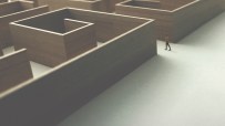 Small figure in a tan coat walks on a white path next to a large, wooden maze, symbolizing business challenges.