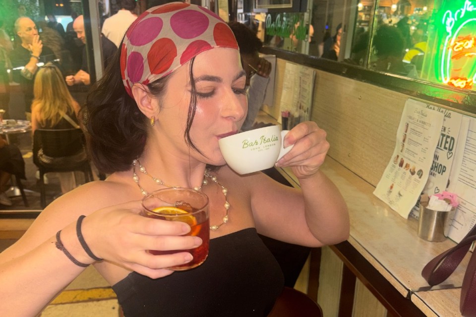 Woman in a polka dot headscarf drinking from a Bar Italia London cup, holding a cocktail.