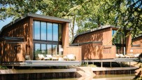 Modern timber-clad lodges, South Lodge The Reeds, with large windows and outdoor decks overlooking a tranquil pond.