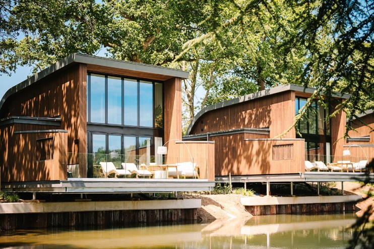 Modern timber-clad lodges, South Lodge The Reeds, with large windows and outdoor decks overlooking a tranquil pond.