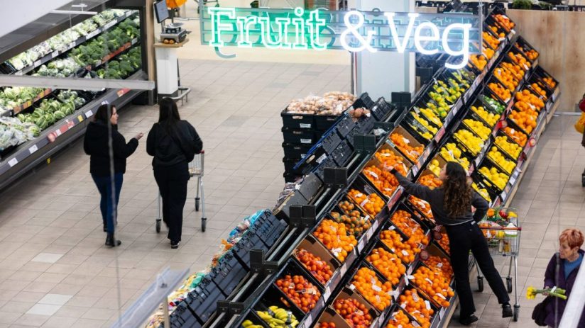 Overhead view of shoppers in a grocery stores fruit and vegetable aisle under a Fruit & Veg sign