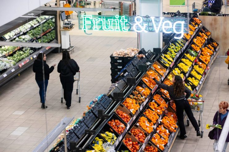 Overhead view of shoppers in a grocery stores fruit and vegetable aisle under a Fruit & Veg sign