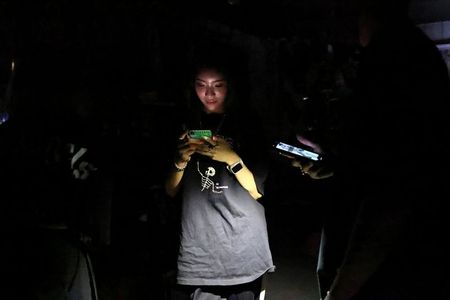 A woman uses her phone while experiencing a blackout due to an outage at a power plant, in Taipei